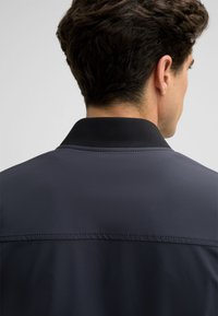 Dunkelblaue Jacke mit schwarzem Kragen. Sanfte Textur und einfaches Design. Verfügt über Nahtdetails auf dem Rücken.