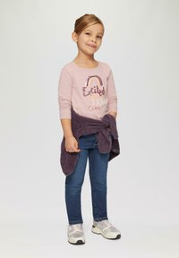 Jasnoróżowa koszula z długim rękawem z napisem "Podekscytowany" i tęczowym motywem, w połączeniu z ciemnoniebieskimi dżinsami i fioletowym, puszystym swetrem zawiązanym w talii.