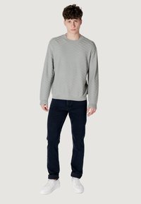 Lichtgrijze, gestructureerde trui met ruitpatroon, ronde hals en geribbelde manchetten, gecombineerd met donkerblauwe jeans en witte sneakers.