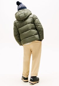 Doudoune vert olive avec capuche, pantalon beige et chaussures noires. La doudoune présente un design matelassé et un bonnet à motif marine.