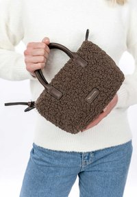 Bolso de mano de terciopelo marrón con una superficie texturizada, asas de cuero y cierre de cremallera. Forma rectangular compacta con un acento de marca.