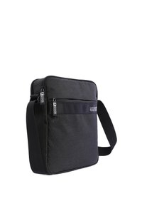 Bandolera negra con una tela texturizada, compartimentos con cremallera, correa ajustable y un acento de logo en el panel frontal.