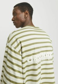 Sudadera de gran tamaño a rayas en verde claro y blanco, con una textura suave y un gran texto gráfico en la parte posterior.