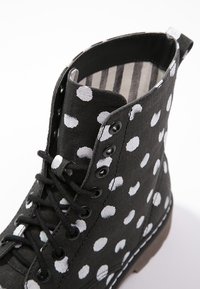 Bottine en toile noire à pois blancs, lacets noirs et œillets métalliques. Intérieur avec un motif rayé. Semelle en caoutchouc.