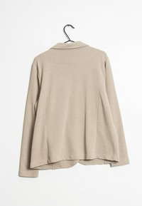 Beige långärmad topp i mjukt material, med krage, rundad nederkant och en något avslappnad passform. Visad bakifrån.