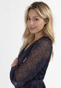 Himmeleväriinen, verkkomainen tummansininen pusero, jossa on pitkät hihat ja V-pääntie. Siinä on herkkiä violetin, vaaleanpunaisen ja sinisen sävyjä teksturoidulla kankaalla.