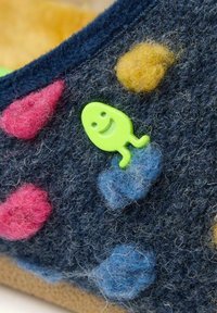 Pantoufle en laine avec une base bleu marine, ornée de points en feutre colorés en rose, jaune et bleu, et d'un accent en plastique vert en forme de poisson souriant.