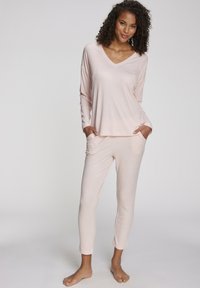 Light pink loungewear set featuring a long-sleeve V-neck top with pockets and matching tapered pants, made from a soft, textured fabric.