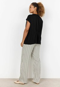 Musthave musta lühike varrukas T-särk tagaküljelt gatheritud; koos beeži ja roheliste geomeetriliste mustritega laia säärega pükstega. Heledad lapikained jalanõud.