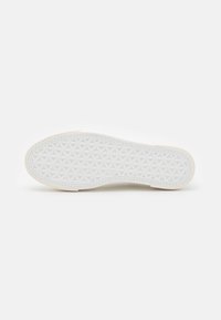 Semelle de sneaker blanche avec un motif texturé présentant un design géométrique de triangles. Matériau en caoutchouc, bords nets et côtés légèrement surélevés.