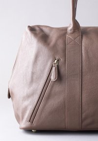 Brown leather bag with a smooth texture, featuring a side zipper, sturdy handles, and flat base for stability. Minimalist design.