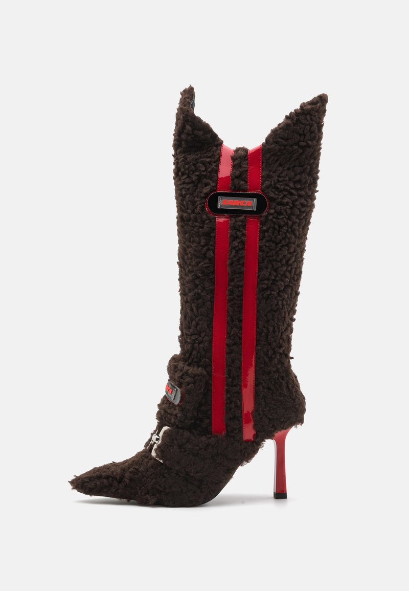 Bota de tacón alto de pelaje marrón con punta afilada, que presenta franjas de charol rojo y un acento de logo en el tobillo. Tejido texturizado.