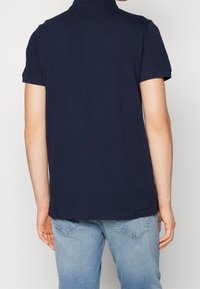 Mörkblå pikétröja med mjuk bomullskänsla, korta ärmar och klassisk krage. Bakdelen har en rak skärning och minimal detaljering.