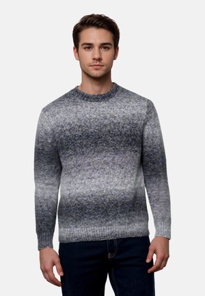 Giovane uomo con maglione a maniche lunghe e scollo rotondo con motivo sfumato grigio e nero, in piedi davanti a uno sfondo chiaro e uniforme.