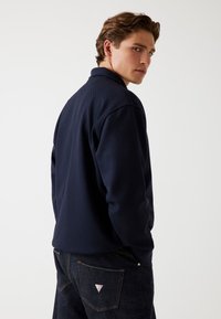 Marineblauwe pullover met geribbelde textuur en een kraag, gecombineerd met donkerdenim jeans met een logo patch op de achterzak.