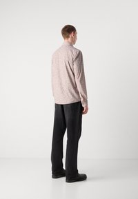 Camicia a maniche lunghe in morbido tessuto rosa chiaro con accenti a motivo foglia sparsi, abbinata a pantaloni neri larghi e calzature nere solide.