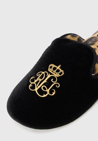 Zapatilla de terciopelo negro con iniciales bordadas en oro y una corona. Forrada con un patrón de leopardo para añadir contraste. Textura suave.