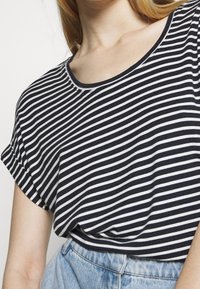 Striped t-shirt featuring navy and white horizontal stripes, a round neckline, and rolled short sleeves; paired with light denim shorts.