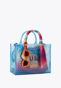 Borsa shopper trasparente blu con motivo a diamante, manico con sciarpa multicolore avvolta e occhiali da sole con strass arancioni appesi davanti.