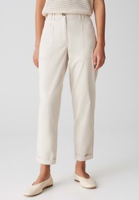 Pantalons couleur crème avec une coupe décontractée, des poches plaquées à l'avant, des ourlets à revers et une texture de tissu légère. Associés à des chaussures légères et arrondies.