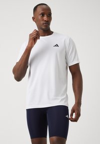 T-shirt athlétique blanc à manches courtes avec un logo noir sur la poitrine, associé à un short ajusté bleu marine. Tissu lisse et léger.