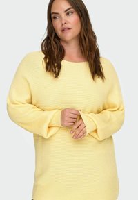 Geltonas megztinis su reljefiniais dryžiais, plačiu iškirptės kaklu, laisvo silueto ir ilgomis rankovėmis. Kūrinys pasižymi plonomis horizontaliomis juostelėmis ir minkšta tekstūra.