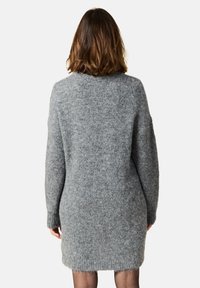 Grå stickad klänning, långa ärmar, rundad halsringning, mjuk textur, midtlånga längd, med avslappnad passform och subtil fransad fåll.