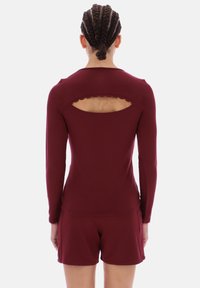 Top burgundiu cu mânecă lungă, cu o decupare în formă de dantelă la spate, textură netedă, asortat cu pantaloni scurți corespunzători.