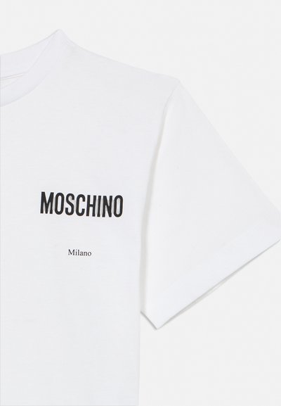 Hvit T-skjorte med kort erme med «MOSCHINO» i fete svarte bokstaver og mindre «Milano»-tekst trykket under på venstre brystområde.