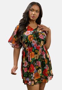 Kukkapuku, joka esittelee mustaa läpinäkyvää kangasta, jossa on kirkkaita punaisia, keltaisia ja vaaleanpunaisia kukkia, V-mallinen pääntie, lyhyet kellohihat ja rypytetty vyötärö.