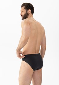 Caleçons pour hommes noirs avec une texture lisse et une taille élastique, présentés sur un modèle vu de côté sur un fond uni.