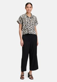 Short-sleeve, leopard print blouse in beige and black, paired with black wide-leg trousers and strappy heels, worn by a model.