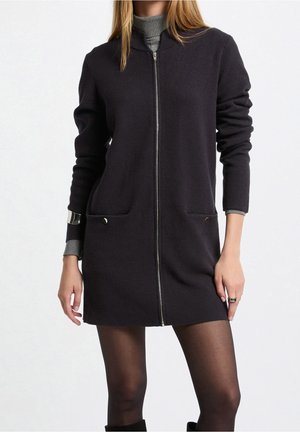 Ciemna sukienka z mieszanki wełny z wysokim kołnierzem, z przodu z zamkiem błyskawicznym i dwoma bocznymi kieszeniami. Posiada długie rękawy i długość do połowy uda. Gładka tekstura.