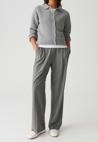 Cardigan gris côtelé avec des boutons sur le devant et une poche, associé à un pantalon gris ample et des baskets blanches.
