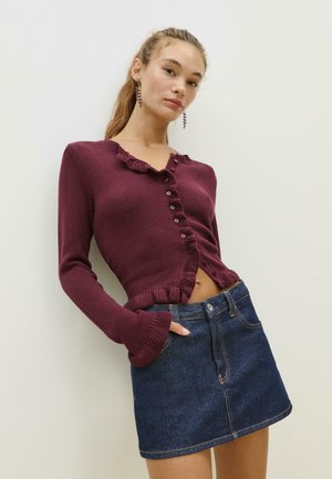 Cardigan tricoté bordeaux avec un col à volants et fermeture à boutons, associé à une mini-jupe en denim foncé avec poches avant.