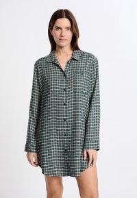 Vestito camicia a quadri verde e crema con maniche lunghe, chiusura con bottoni e una tasca sul petto. Texture morbida e vestibilità rilassata.