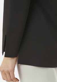 Zwarte blouse met lange mouwen en een zijsplit bij de manchet. Glad textuur met een rechte snit. Gecombineerd met een lichte onderkant.