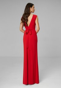 Czerwona długa suknia z podwójnym dekoltem w kształcie V, krótkimi rękawami i wiązaniem w talii. Wykonana z gładkiego materiału, posiada zwiewny krój spódnicy.