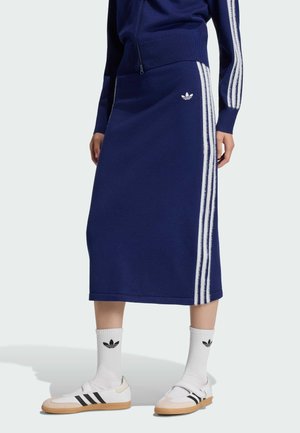 Marineblauer Rock mit weißen Seitenstreifen und Adidas-Logo, kombiniert mit passender Jacke, weißen Adidas-Socken und weißen Sneakers mit schwarzen Streifen.