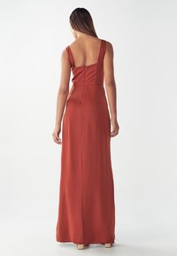 Langes, rostfarbenes Kleid mit einem dezenten Reißverschluss im Rücken, breiten Trägern und einem taillierten Design, das bis zum Boden fließt. Glatte Textur über die gesamte Fläche.