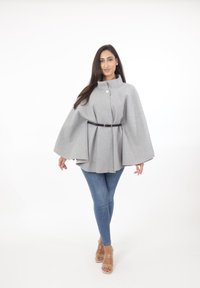 Capa de mezcla de lana gris con un cuello alto y cierre de botón delantero, ceñida a la cintura con un cinturón negro, usada sobre unos jeans azules.