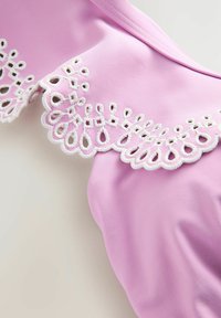Roze stof met een witte kanten rand met golfpatroon en druppelvormige uitsparingen. De textuur is glad, met decoratieve stiksel langs de kant.