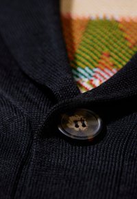 Primo piano di un cappotto di tessuto scuro con bottoni, con un indumento lavorato a maglia multicolore visibile sotto.