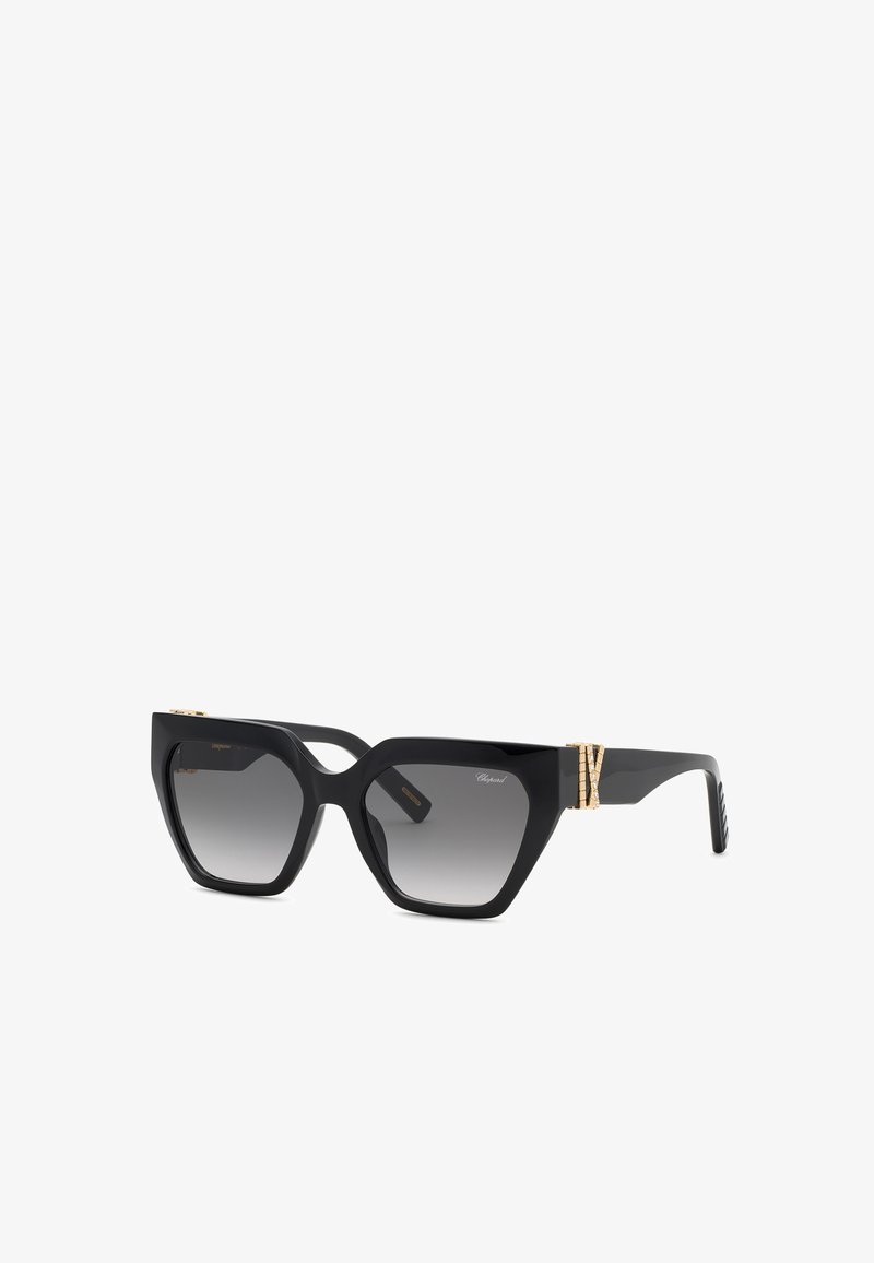 Lunettes de soleil angulaires noires forme œil de chat avec verres gris dégradés et détail décoratif doré sur les branches.