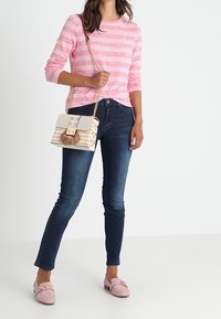 Gestreifter rosa Pullover, dunkle Jeans, rosa Slipper mit dekorativer Hardware und eine kleine cremefarbene Handtasche mit Kettenriemen und Quaste.