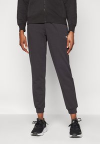 Gray sweatpants with elastic cuffs, made from a soft material. Features a small white logo on the left side and worn with black sneakers.