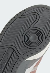 Gray rubber sneaker outsole with a wave pattern, circular detail, and contrasting white accent. Textured grip surfaces for traction.