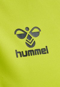 Czarne stylizowane logo pszczoły z detalami w kształcie jodełki nad małymi literami „hummel” na jasnym, żółtym, teksturowanym tle z tkaniny.