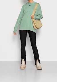 Person med mintgrön oversized sweatshirt, svarta tighta byxor med frontslitsar, beigefärgade klumpiga stövlar och en beige axelväska.