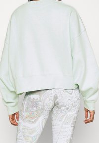 Ljusgrön oversized sweatshirt med en cropped nederkant och sänkta axlar, kombinerad med vita leggings med ett färgglatt abstrakt mönster.